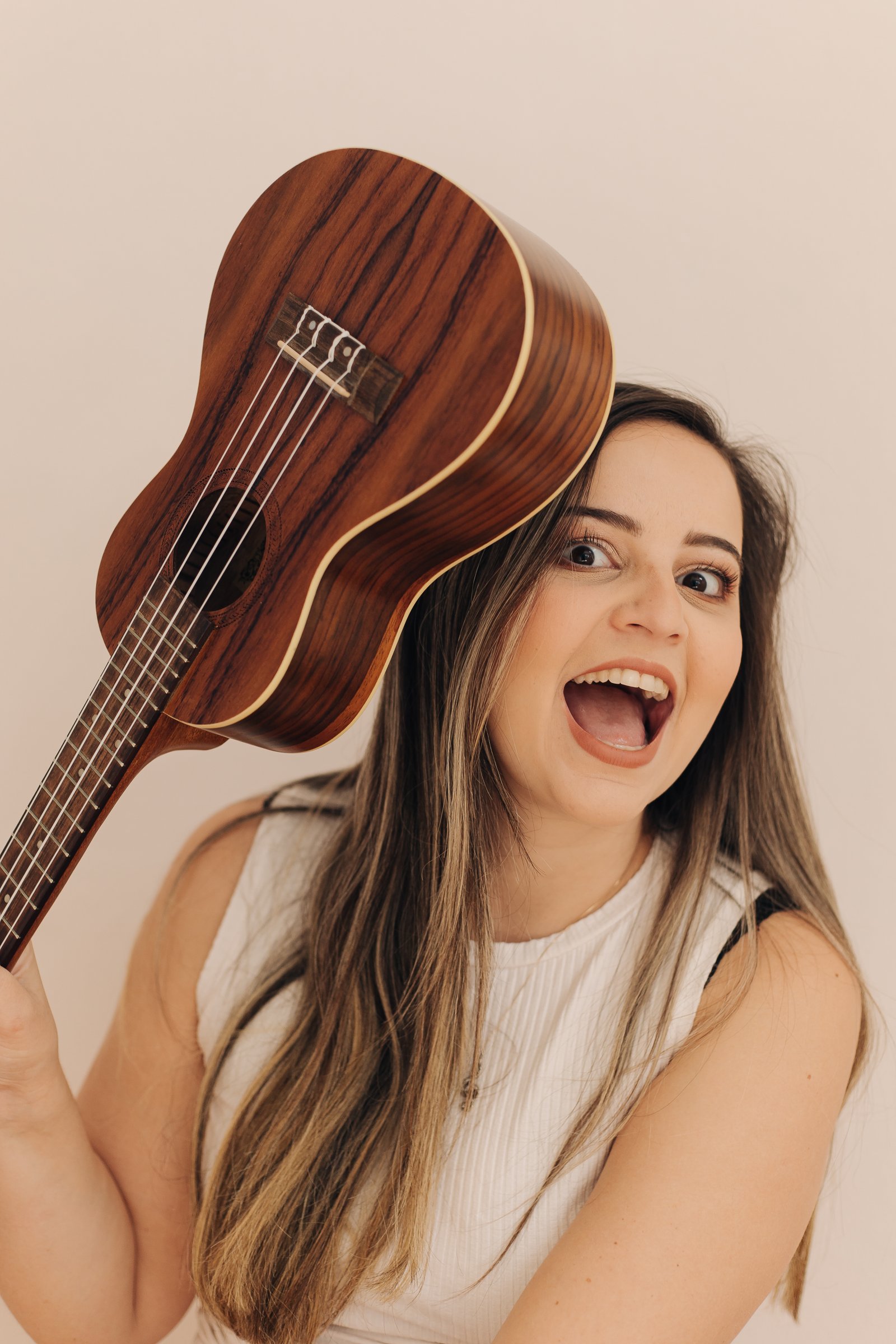 Isa Oliveira sorrindo com um ukulele ao lado do rosto, retrato caloroso